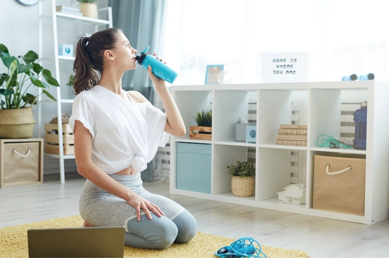 Workout tips for busy moms: a woman on her yoga mat drinking water in a bright lit room