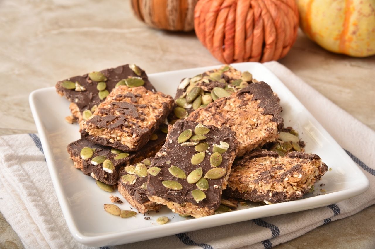 Chocolate and pumpkin seed bars on a white plate with crocheted pumpkins in the background